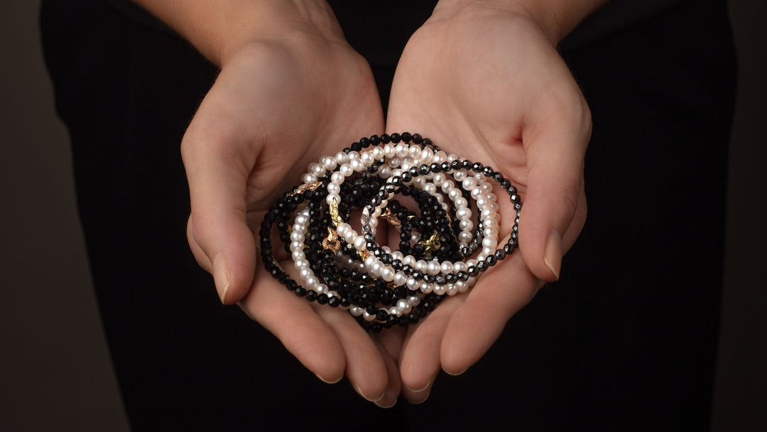Woman's hands hold stack of REALM beaded Bond Bracelets in pearl, black agate and hematite