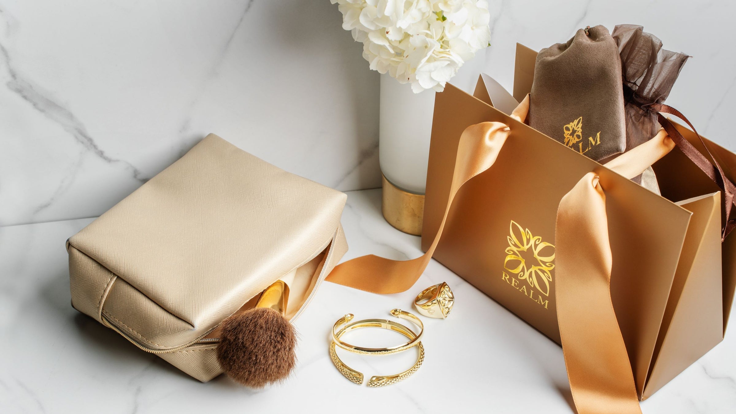 Luxe gift packaging from REALM on vanity with cosmetic case and gold jewelry.