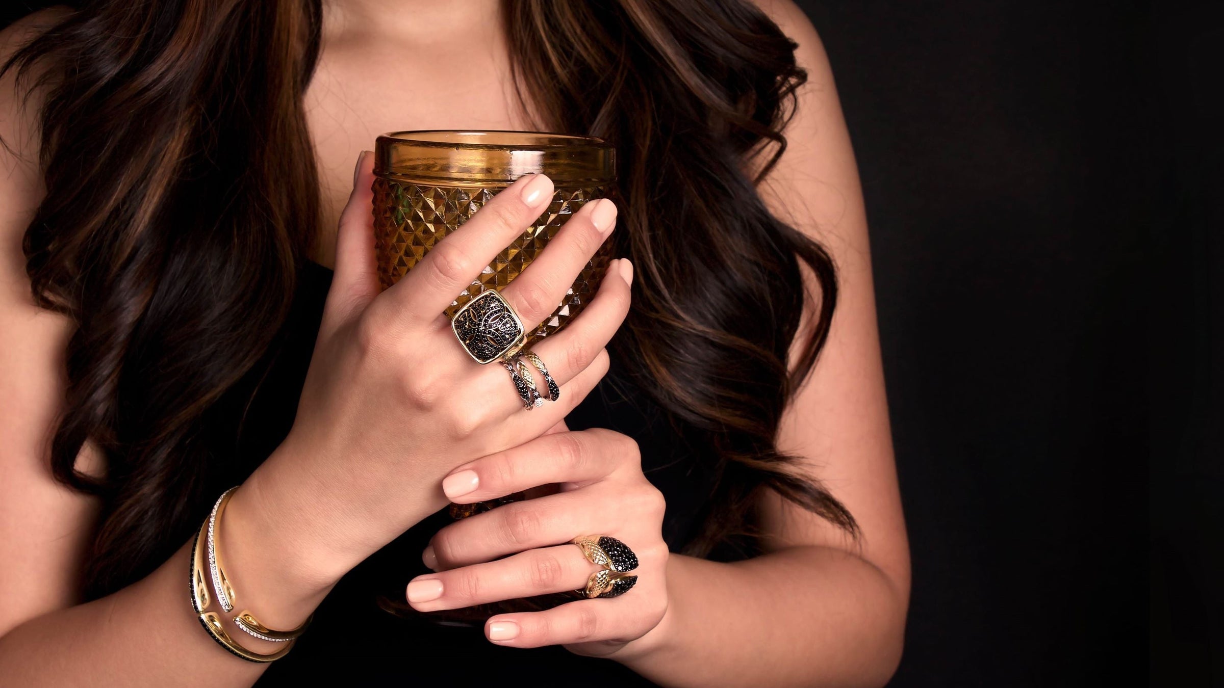 woman holding amber glass wearing dramatic gold and black cz jewelry from REALM