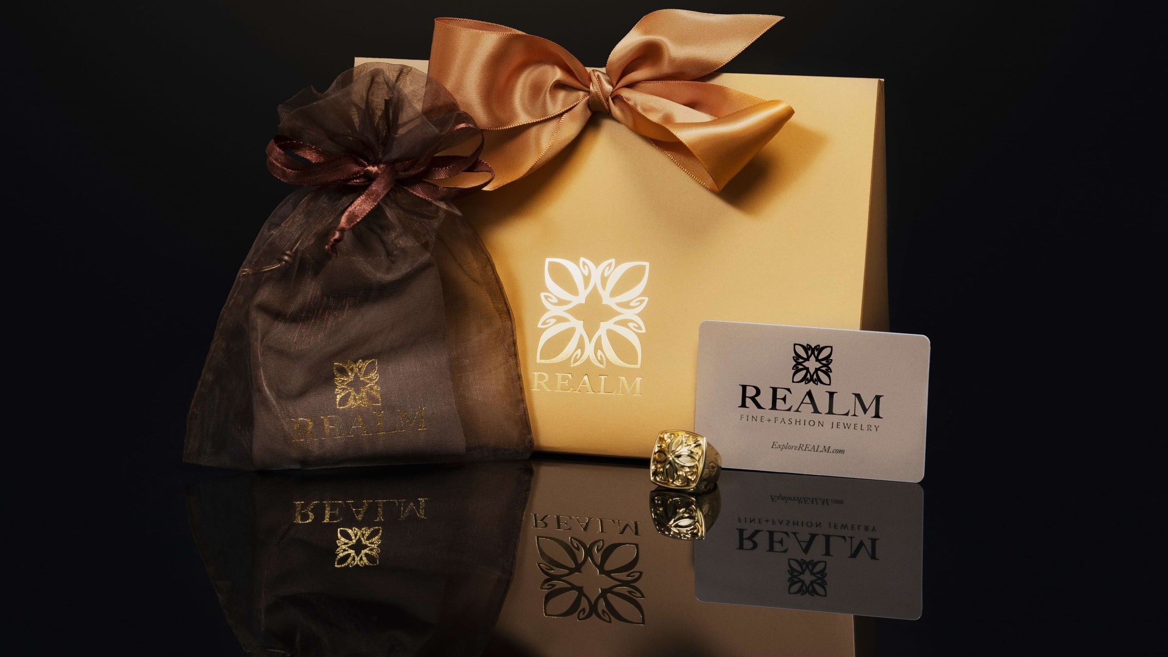 REALM gift card with gold logo gift bag, satin bow, organza bag and suede jewelry pouch — the complete REALM gift experience featuring the Empress ring.