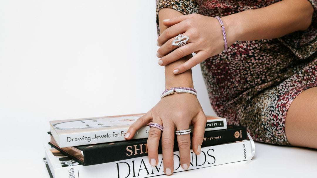 Person wearing multiple rings on a stack of books with a white background