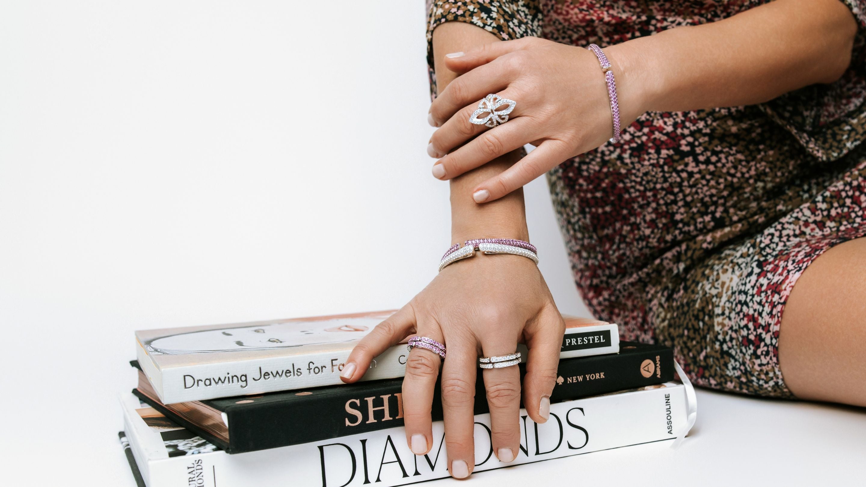 Person wearing multiple rings on a stack of books with a white background