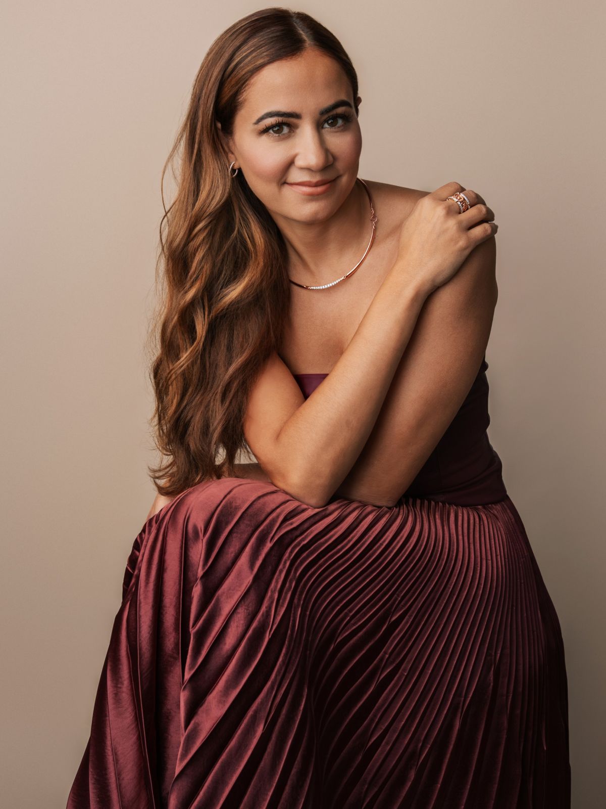 Woman wearing a burgundy pleated dress and rose gold jewelry