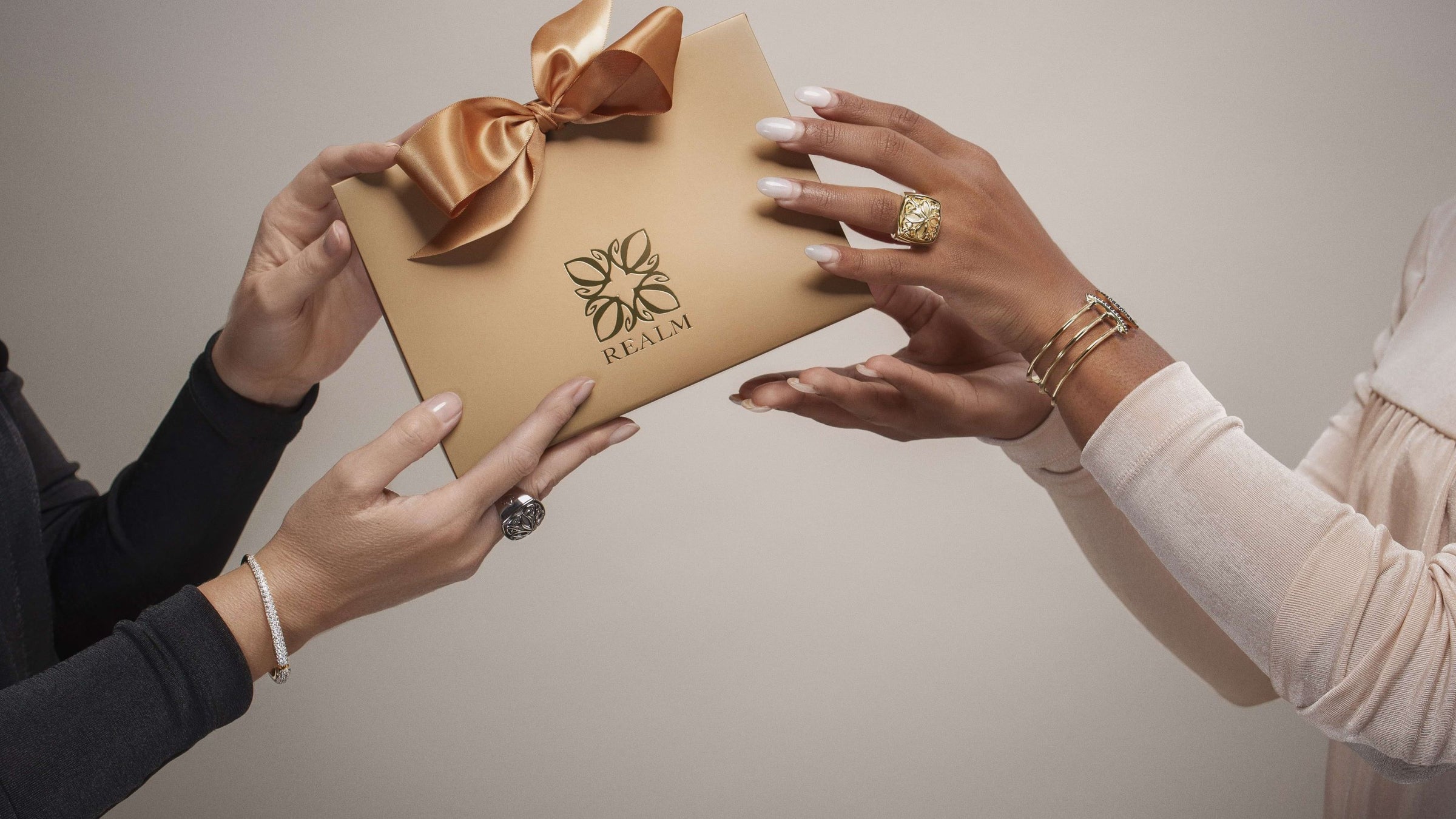 Women with bracelets and rings handing each other REALM gift gold bag