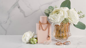 pretty rose gold jewelry with vase of white roses and pink perfume bottle