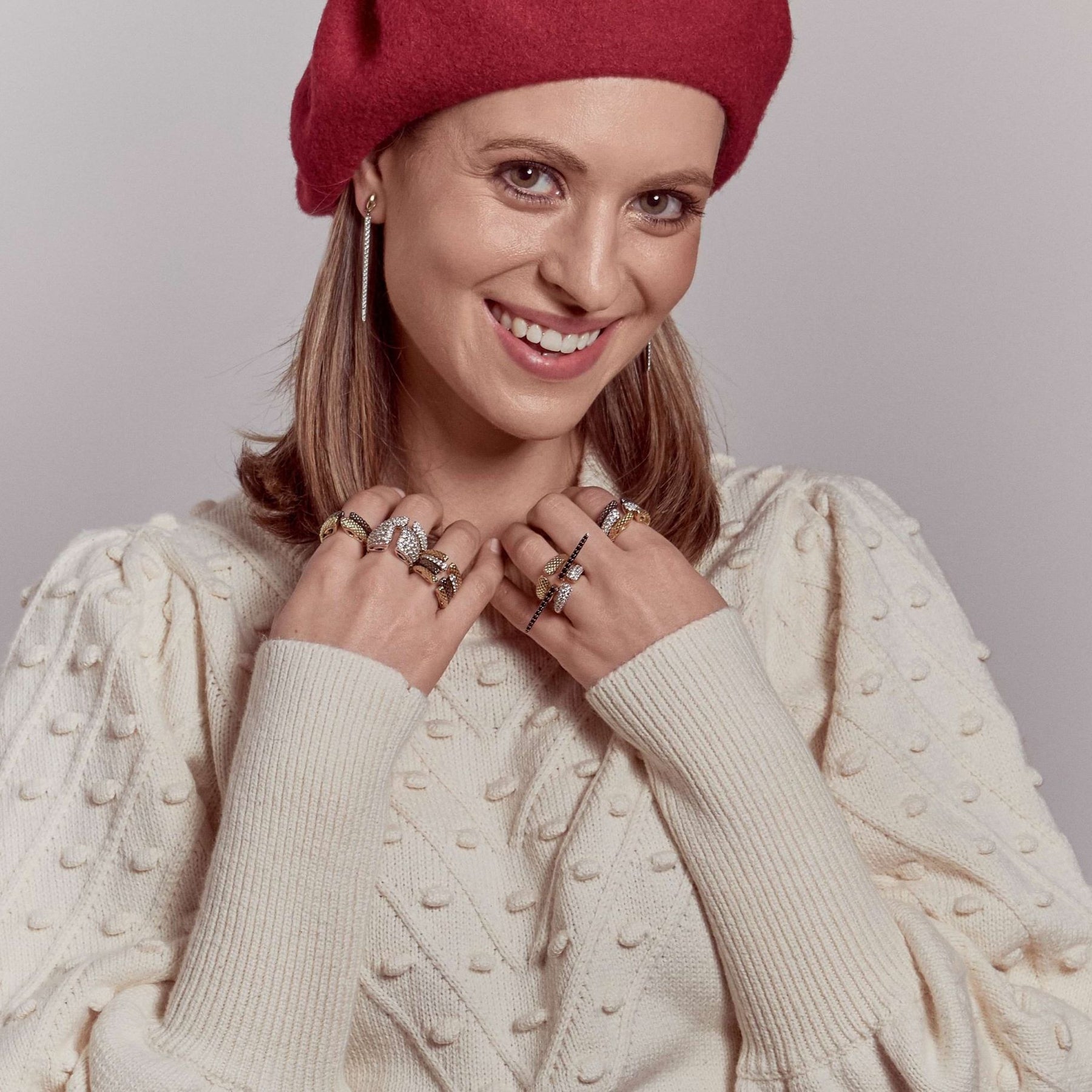 Woman in red beret and cream sweater wearing array of REALM stack rings in gold, silver, rose gold, black ruthenium and cubic zirconia.