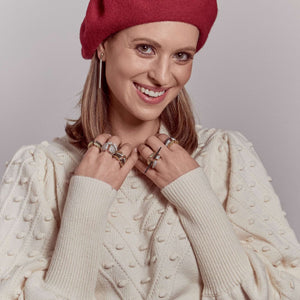 Woman in red beret and cream sweater wearing array of REALM stack rings in gold, silver, rose gold, black ruthenium and cubic zirconia.